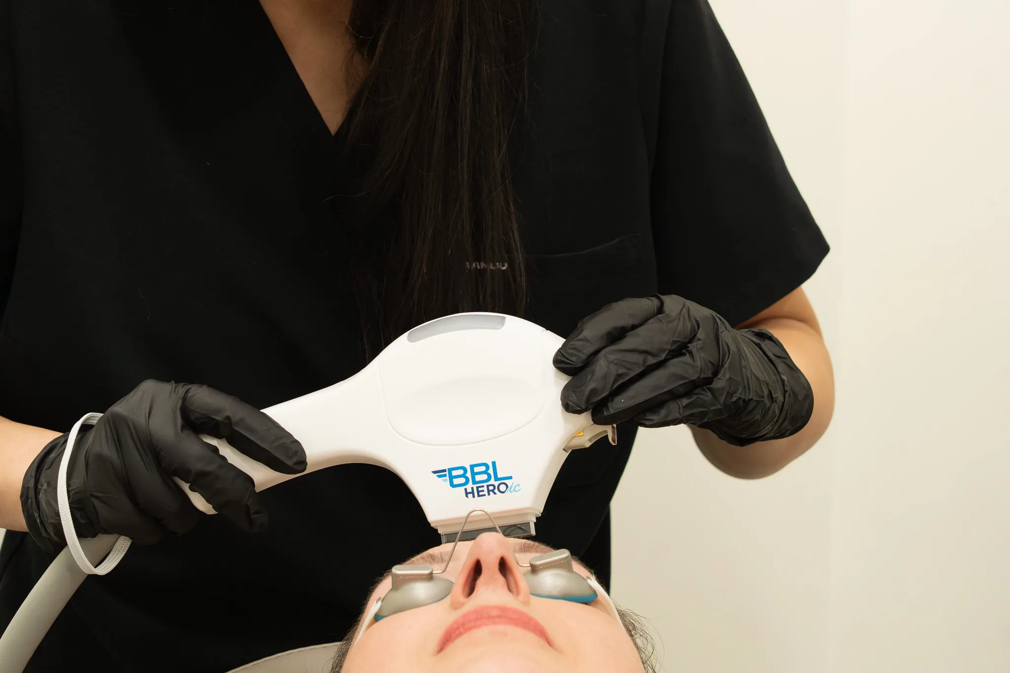 The BBL HEROic handpiece held above a patient wearing protective eye shields.
